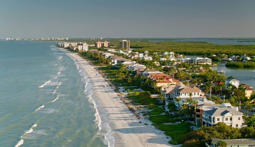 Aerial view of Bonita Springs coastline with beachfront homes and lush greenery.